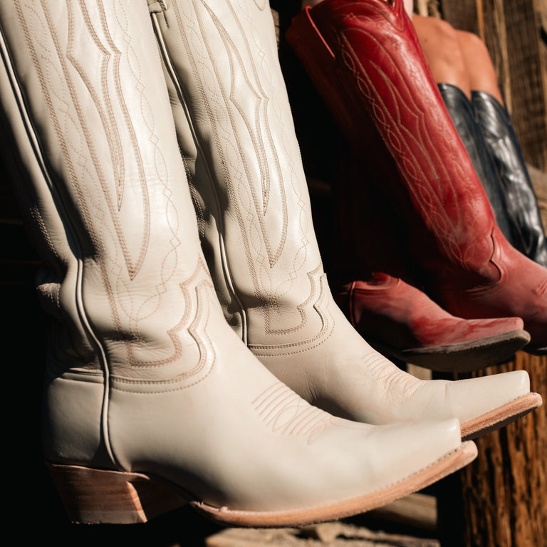 Row of cowboy boots in various colors including white, red, and black on a wooden surface.
