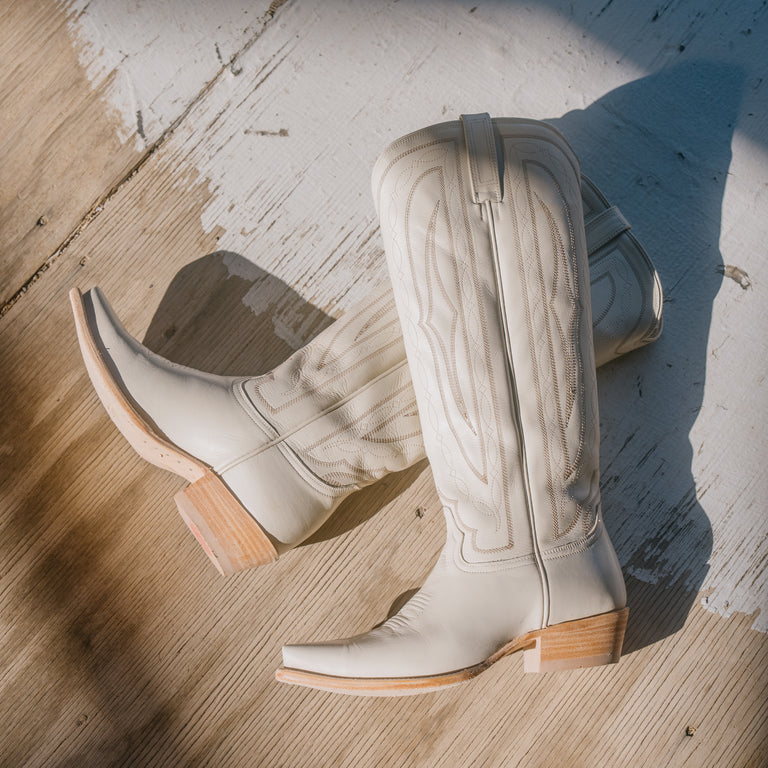 Pair of white cowboy boots with wooden soles on a wooden floor.