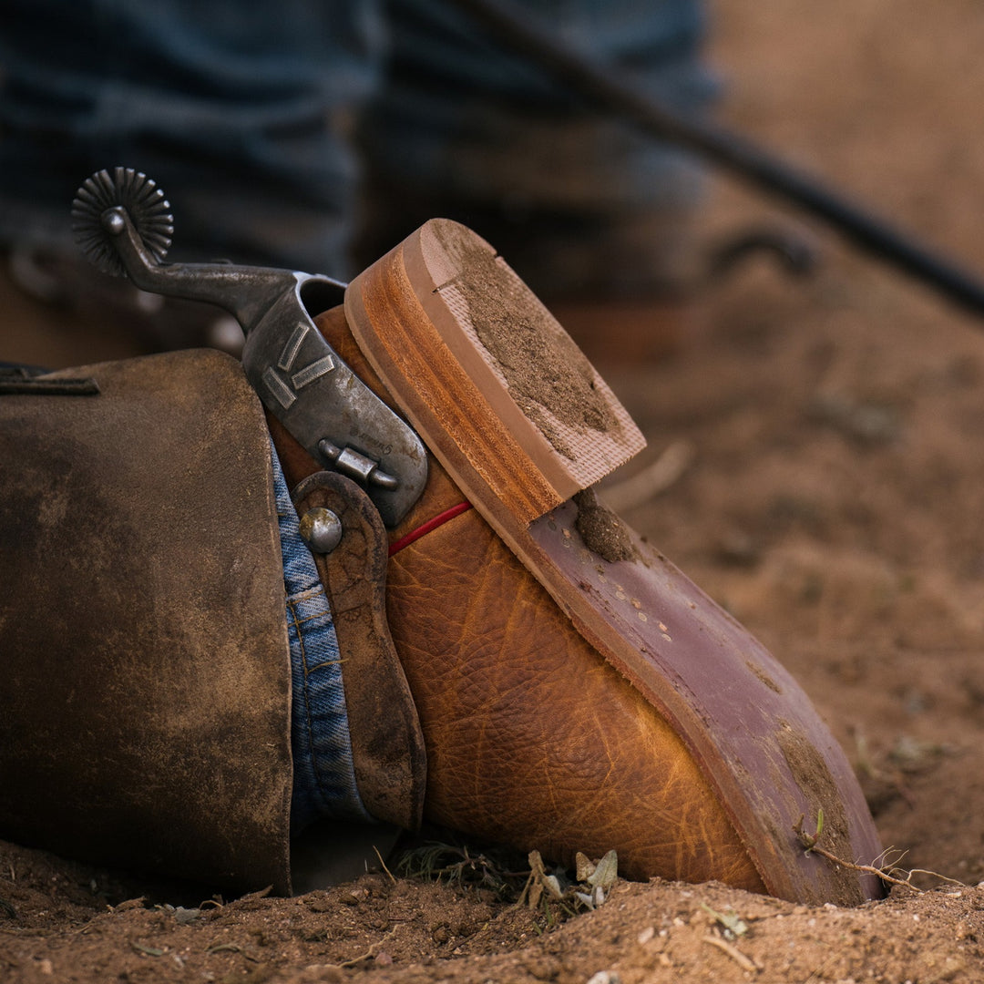 Close up lifestyle image of person wearing cowboy boot with a spur, with toe digging into dirt