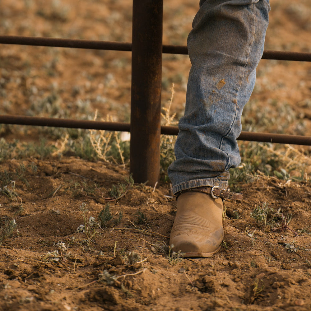 Cowboy boot standing in dirt with fence bars in background