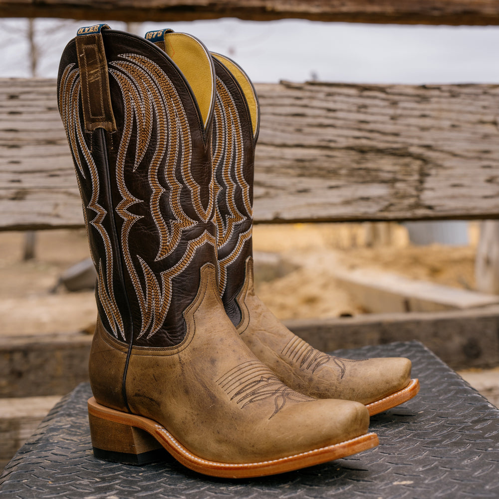Pair of brown cowboy boots with intricate designs on a wooden surface.