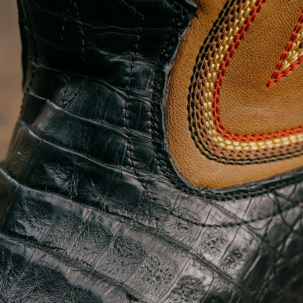 Close in detail of black caiman leather on cowboy boot with black, yellow and red stitching