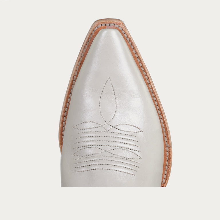 White pointed-toe cowboy boot toe with brown leather trim on a light gray background